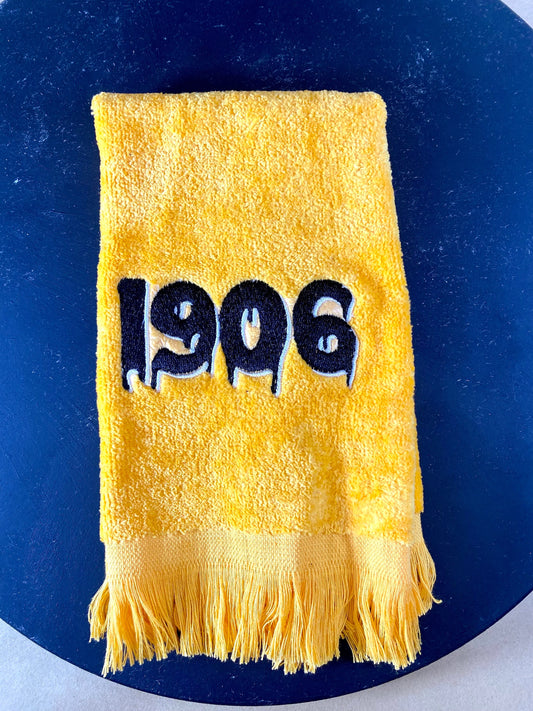 Gold plush velour towel embroidered with a dripping 1906 in black with white accent.