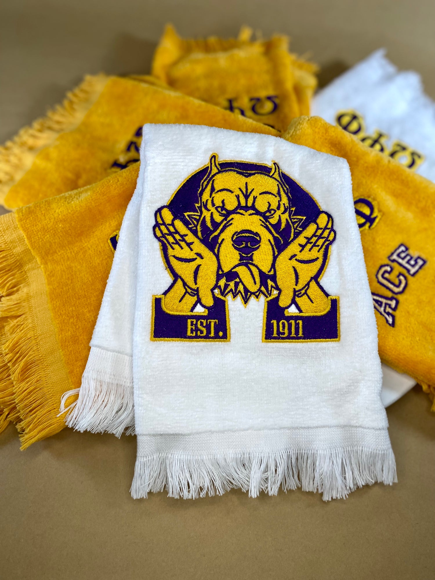 White towel embroidered with purple and gold dog, hooks, and Est. 1911.
