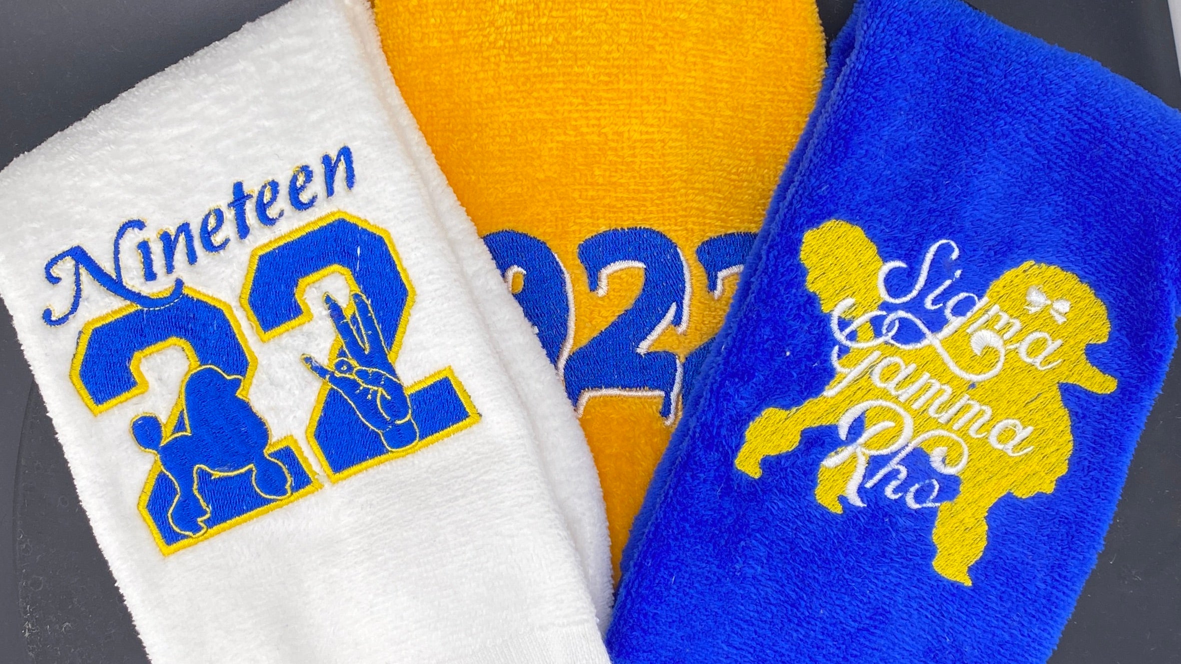 Sigma Gamma Rho Leisure Luxe Towels. Our Legacy Towel in White, Our Drip Towel in Gold and our Poodle Towel in Rhoyal Blue.