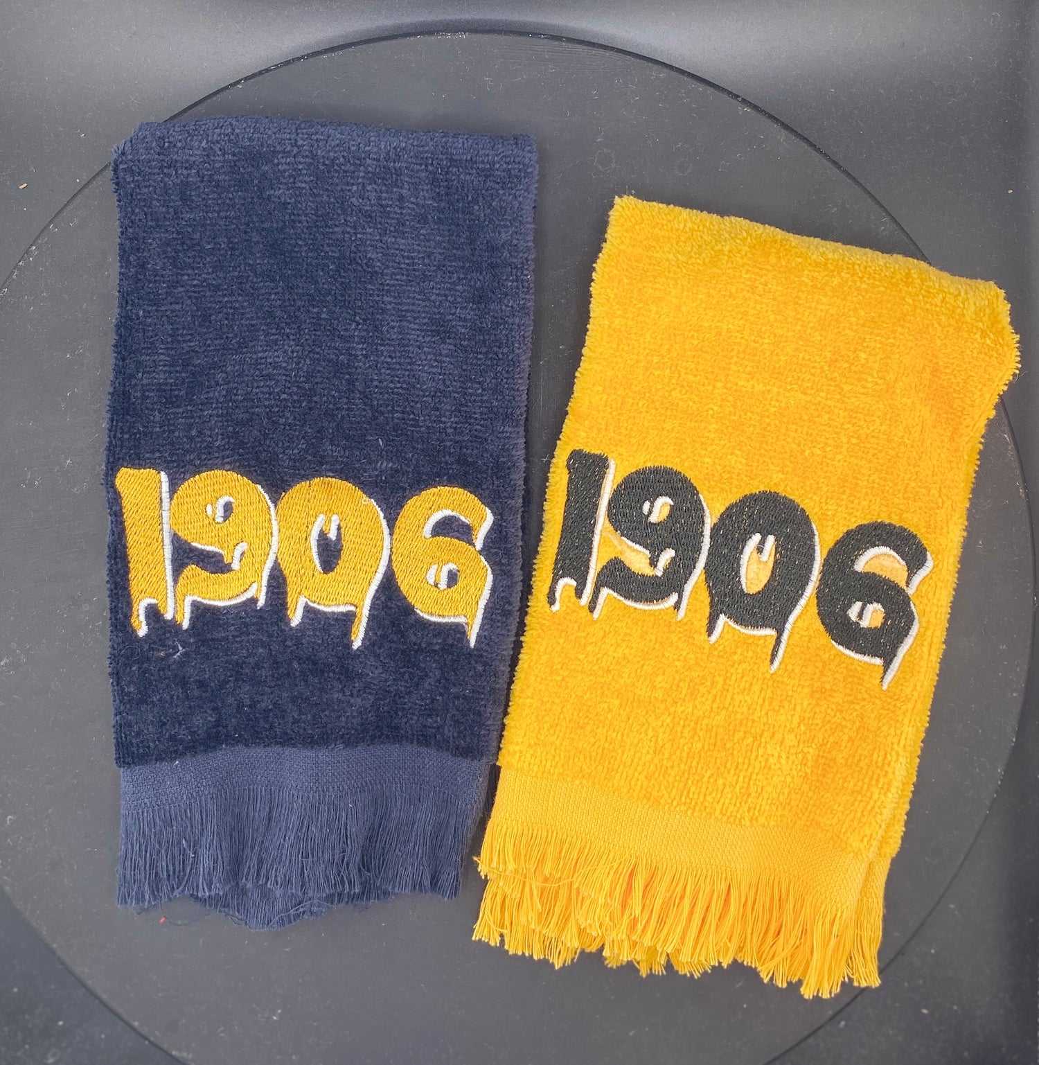 Two Stroll Towels, one black and one gold, with '1906' embroidered on them representing Alpha Phi Alpha.