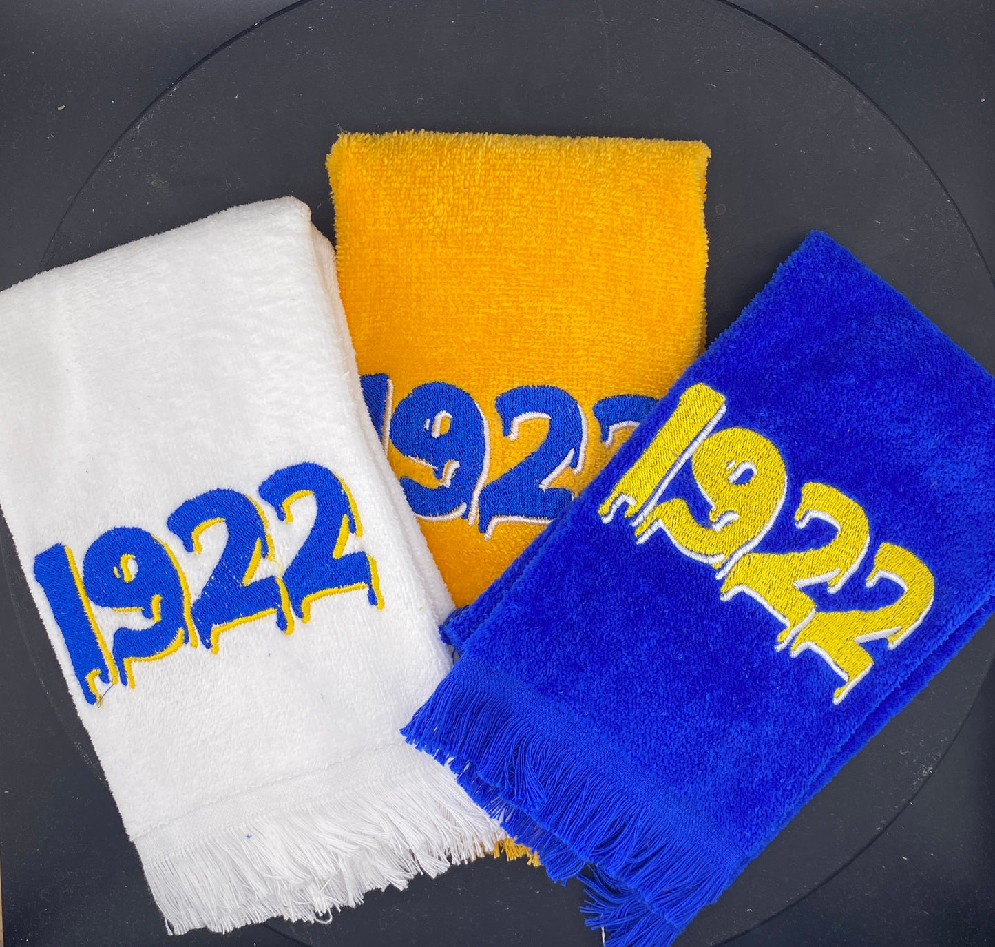 White, Gold, and Rhoyal Blue plush velour towels embroidered with a dripping 1922 in contrasting colors. 