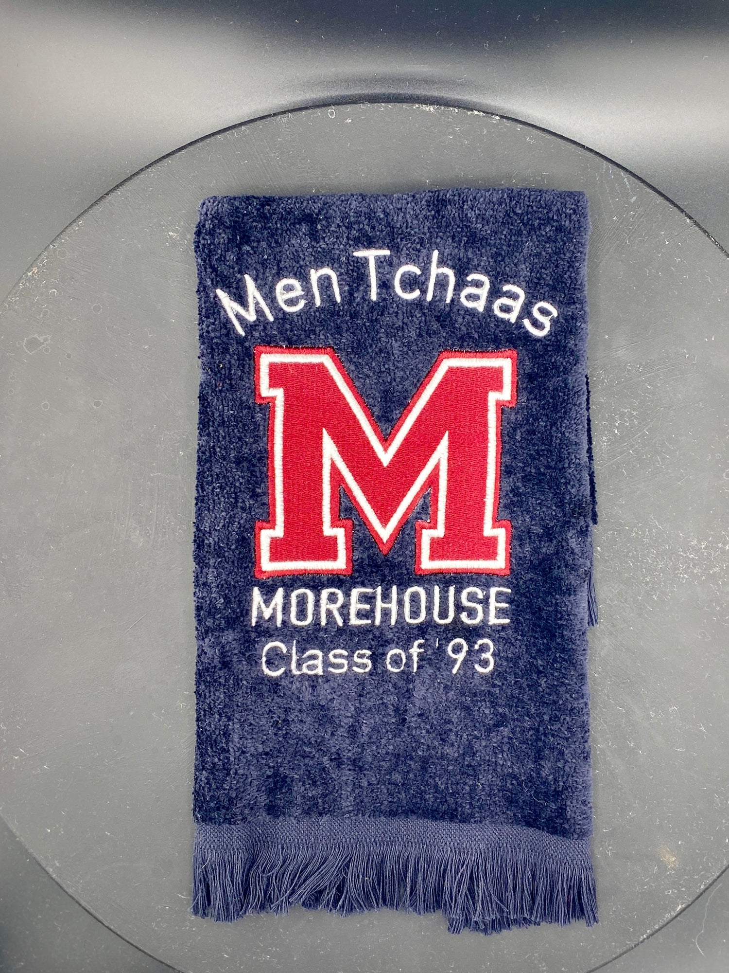 a black velour fringed fingertip towel with a maroon M logo for Morehouse college. the towel is customized with the graduates name and graduating class. 