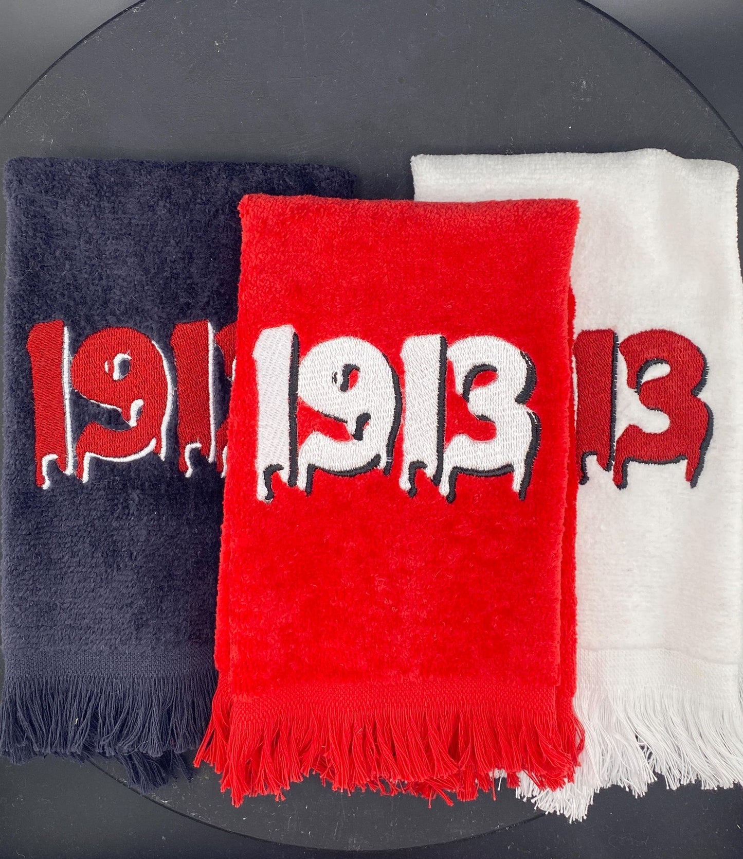 3 plush velour towels in black, red, and white. Each is embroidered with a dripping 1913 in contrasting colors. 