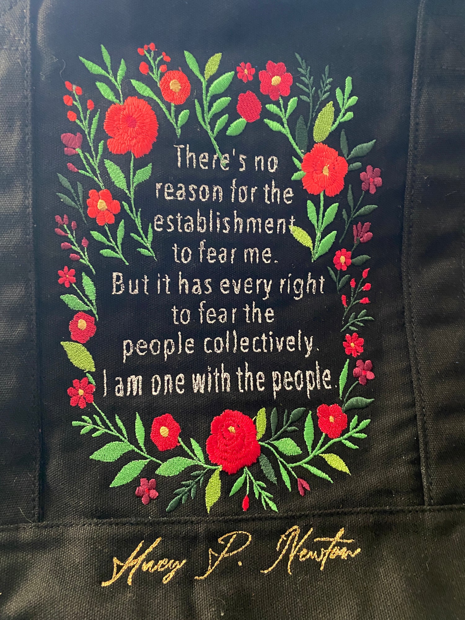 "There's no reason for the establishment to fear me. But it has every right to fear the people collectively - I am one with the people." on a black tote with a red wildflower frame. 
