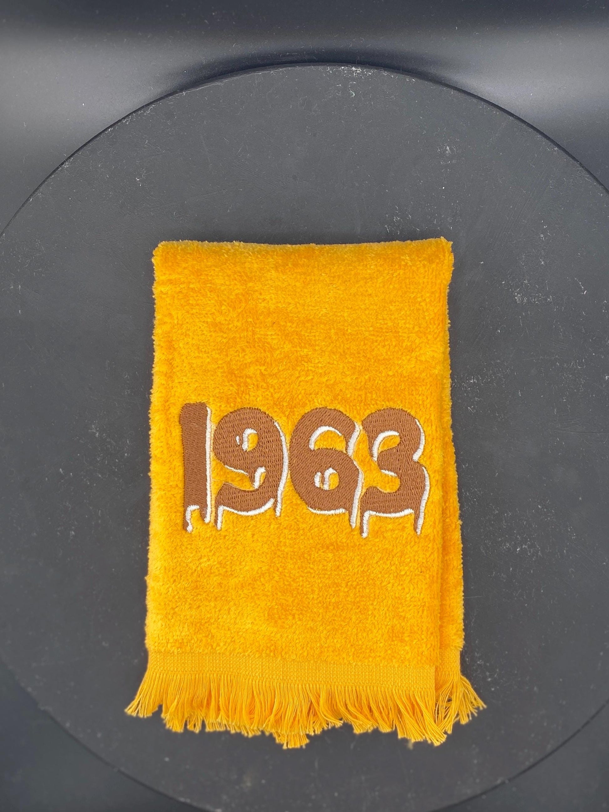 Gold plush velour towel embroidered with a dripping 1963 in brown with white accent. 