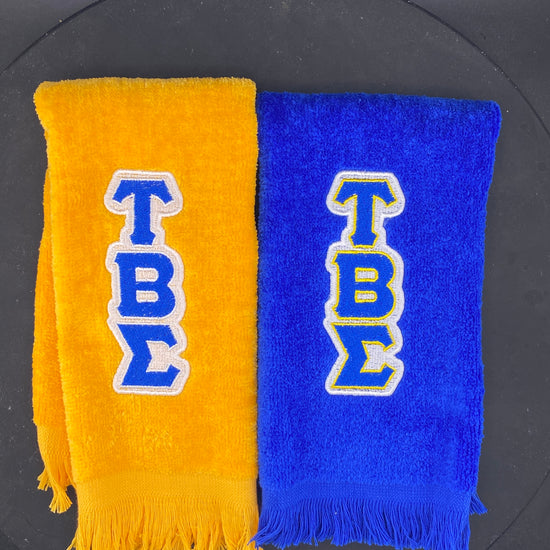 a Royal Blue and a Gold Leisure Luxe Stroll Towel embroidered with Tau Beta Sigma letters. 