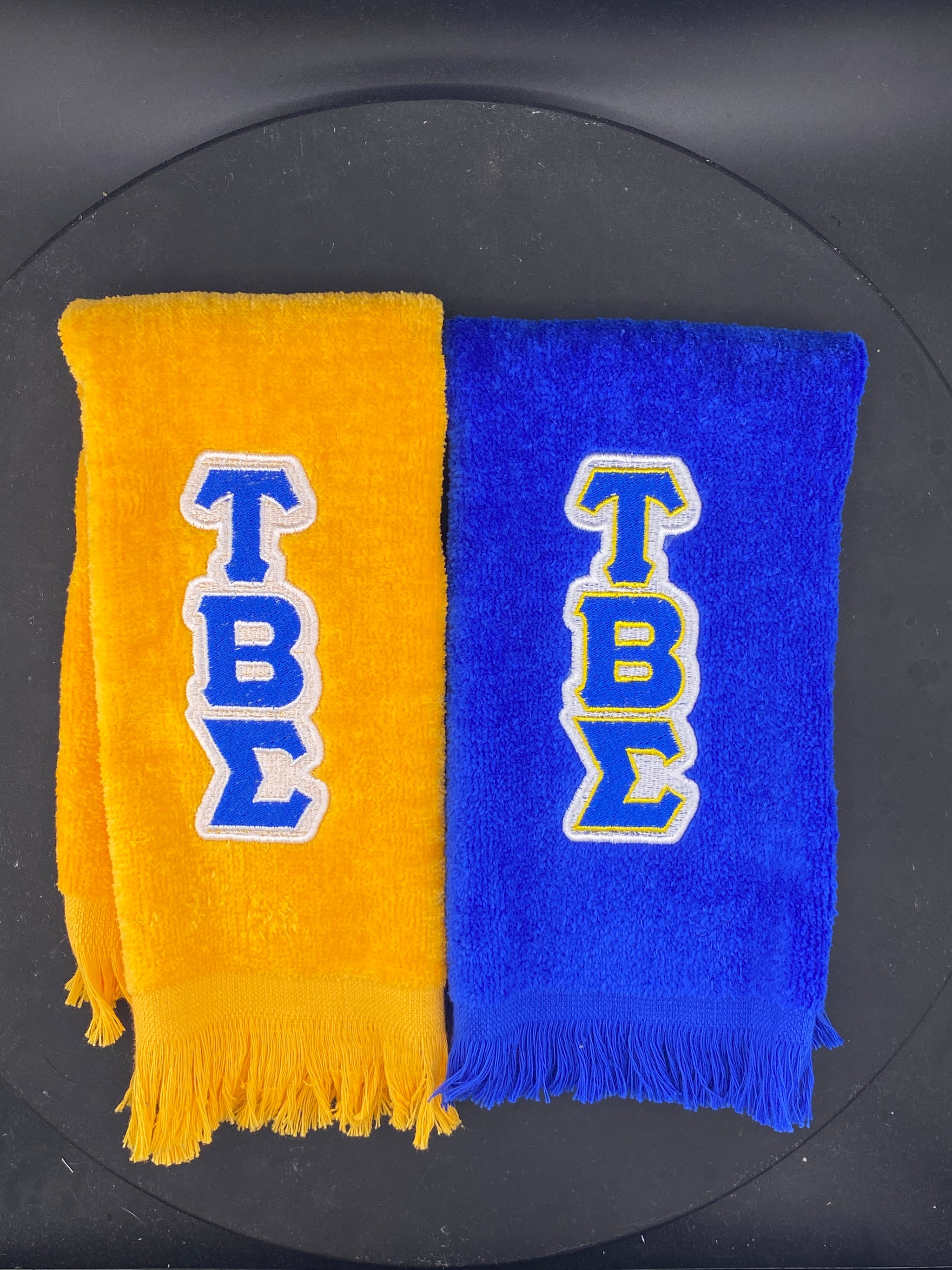 a Royal Blue and a Gold Leisure Luxe Stroll Towel embroidered with Tau Beta Sigma letters. 