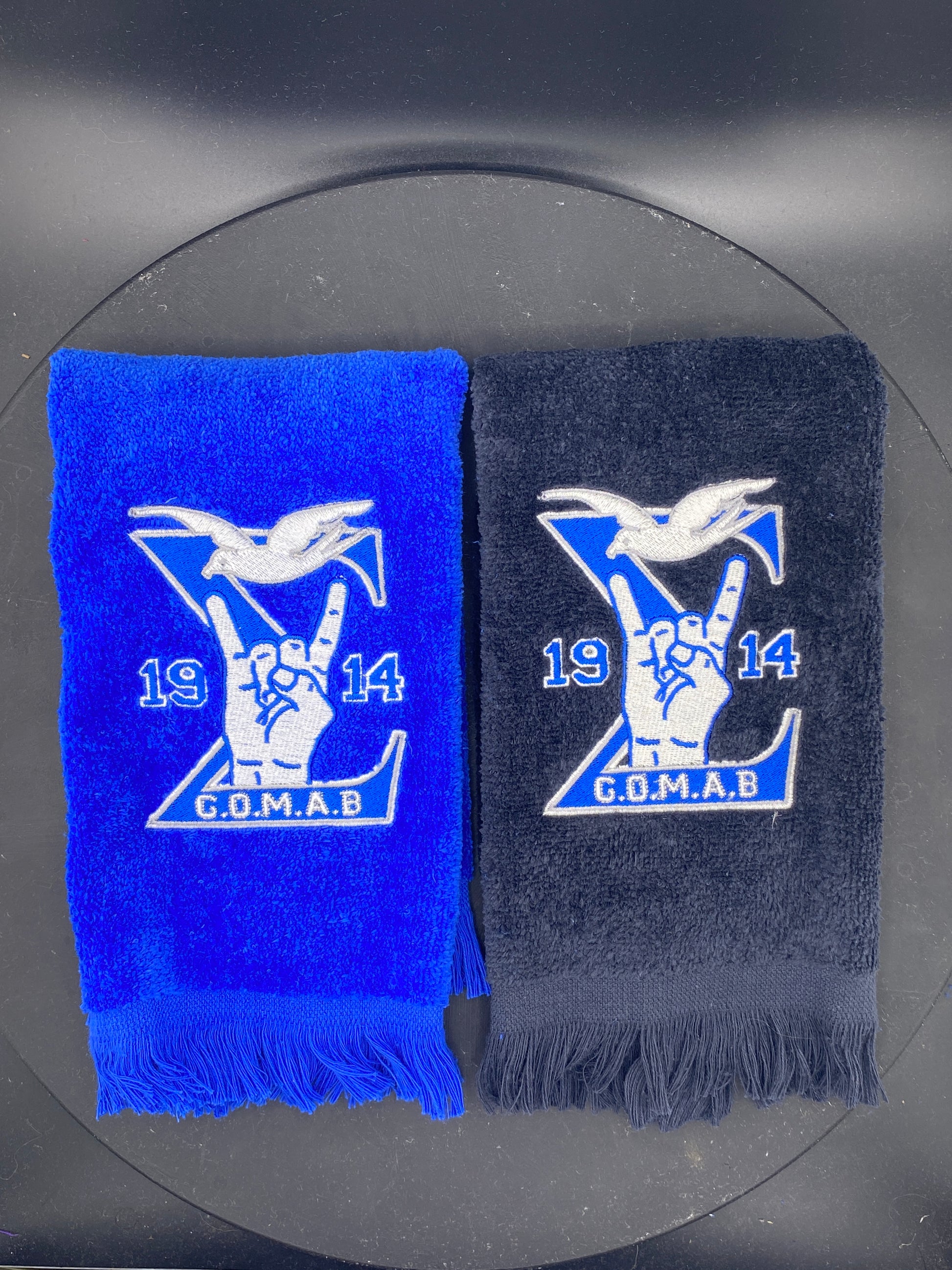 Black and royal blue Stroll Towel with a Sigma, 1914, handsign, dove and GOMAB embroidered in while and silver.  